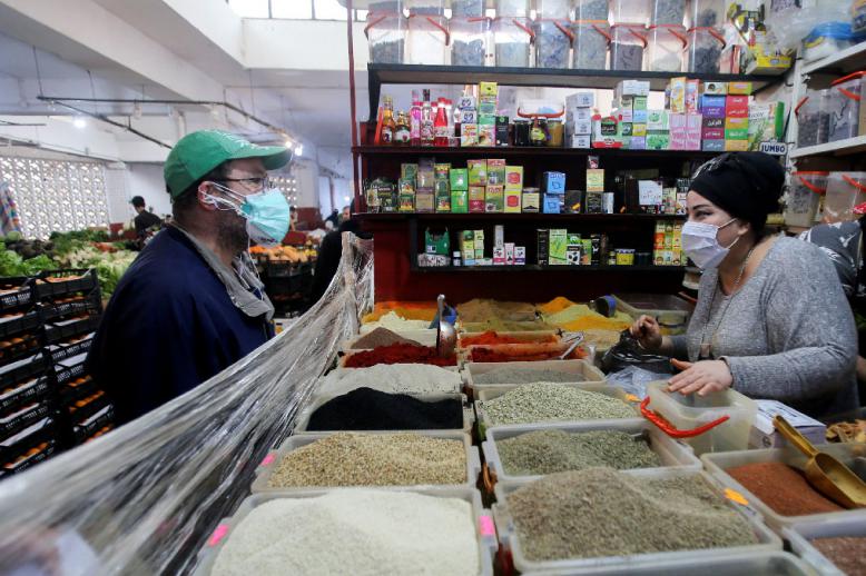 A vendor wearing a protective face mask serves a customer inside her shop in Algiers