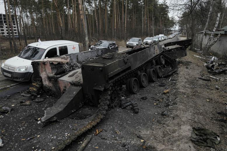 Cars drive past a destroyed Russian tank as a convoy of vehicles evacuating civilians leaves Irpin, on the outskirts of Kyiv