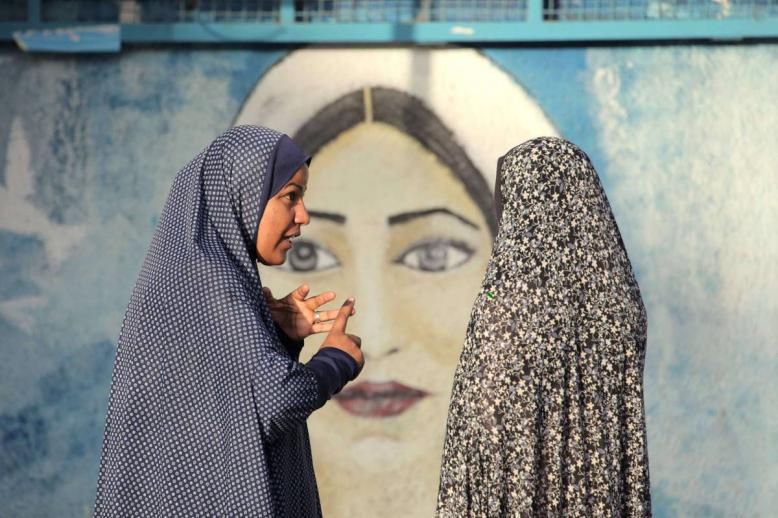 فلسطينيات أمام جدارية للمرأة الفلسطينية في غزة
