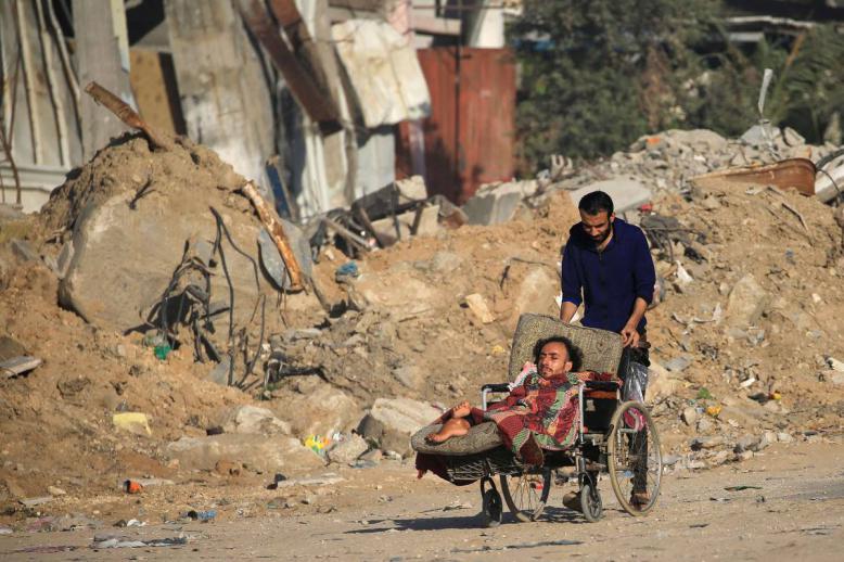فلسطيني يدفع كرسيا متحركا لمعاق في غزة