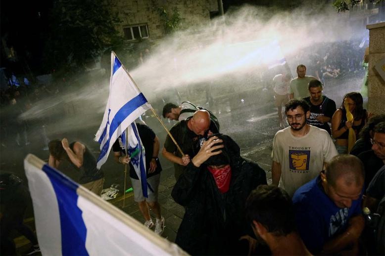 Protesters take cover from a water cannon used from a law enforcement vehicle in Jerusalem