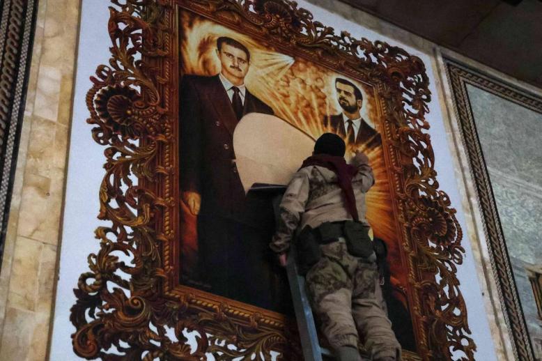 مقاتلو المعارضة يمزقون لوحة للرئيس بشار الأسد وأخيه الراحل باسل في مطار حلب