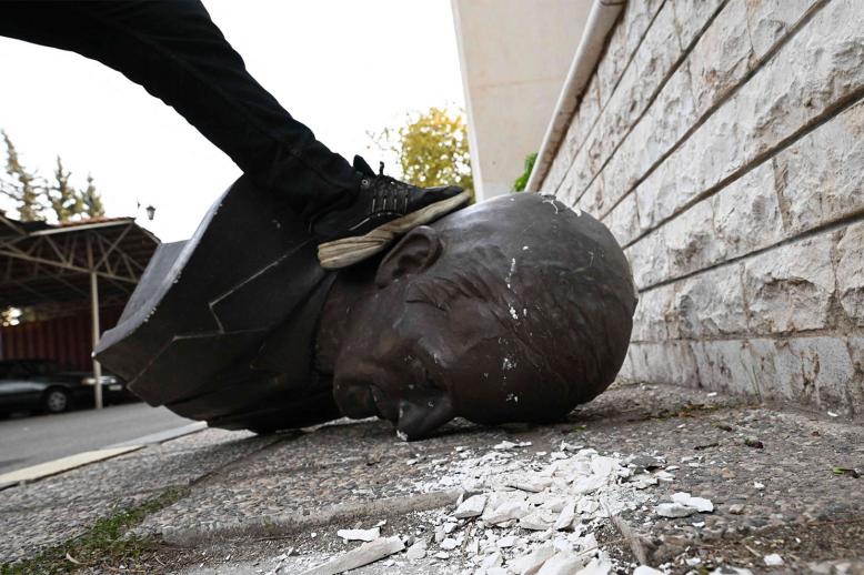 An anti-government fighter steps on the head of a broken statue of late Syrian president Hafez al-Assad