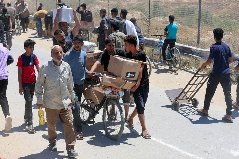 Palestinians walk with aid supplies which they received from the US-backed Gaza Humanitarian Foundation, in the central Gaza Strip