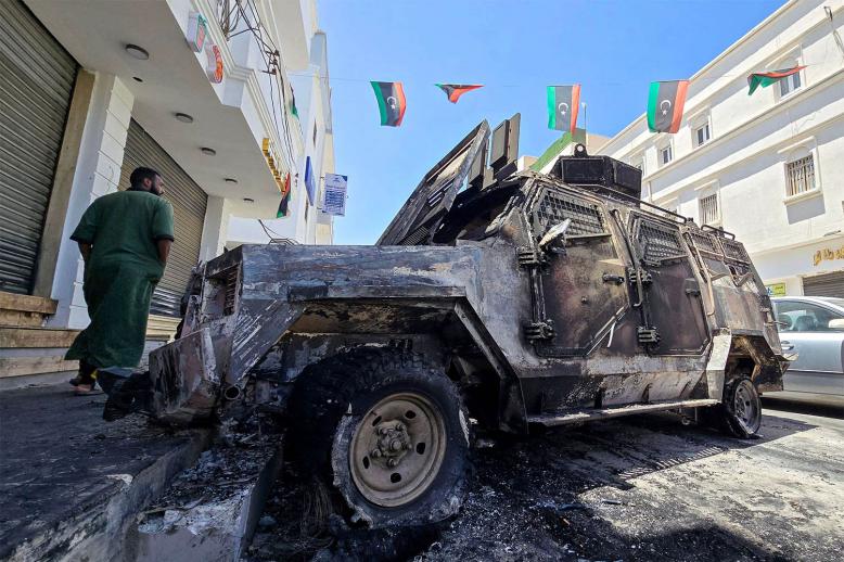 A man walks past a car that was destroyed during overnight clashes in the southern district of Abu Salim in Tripoli