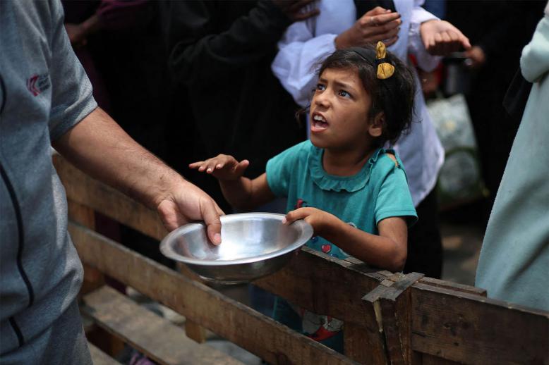 A Palestinian girl holds an empty pan at a hot meal distribution point in Nuseirat in the central Gaza Strip