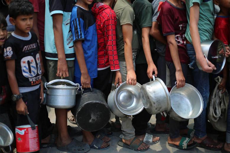 Palestinian boys carry pots as the queue at a hot meal distribution point in Nuseirat in the central Gaza Strip
