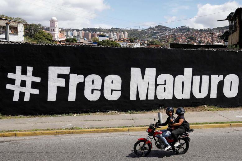 A motorcyclist passes in front of a mural that says Free Maduro in Caracas