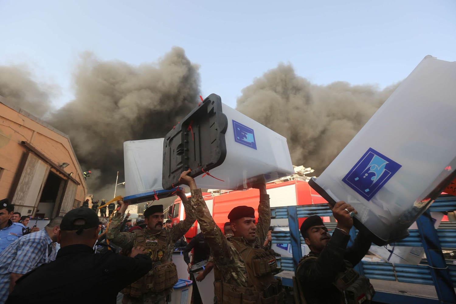 رجال أمن عراقيون ينقلون صناديق الاقتراع بعيدا عن الحريق
