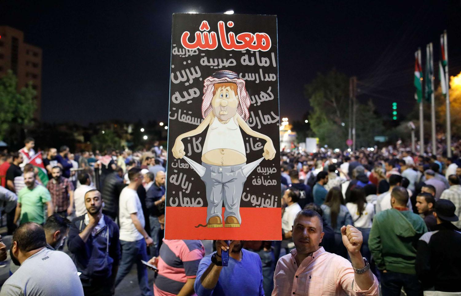 متظاهر أردني يرفع لافتة بالقرب من مقر الحكومة