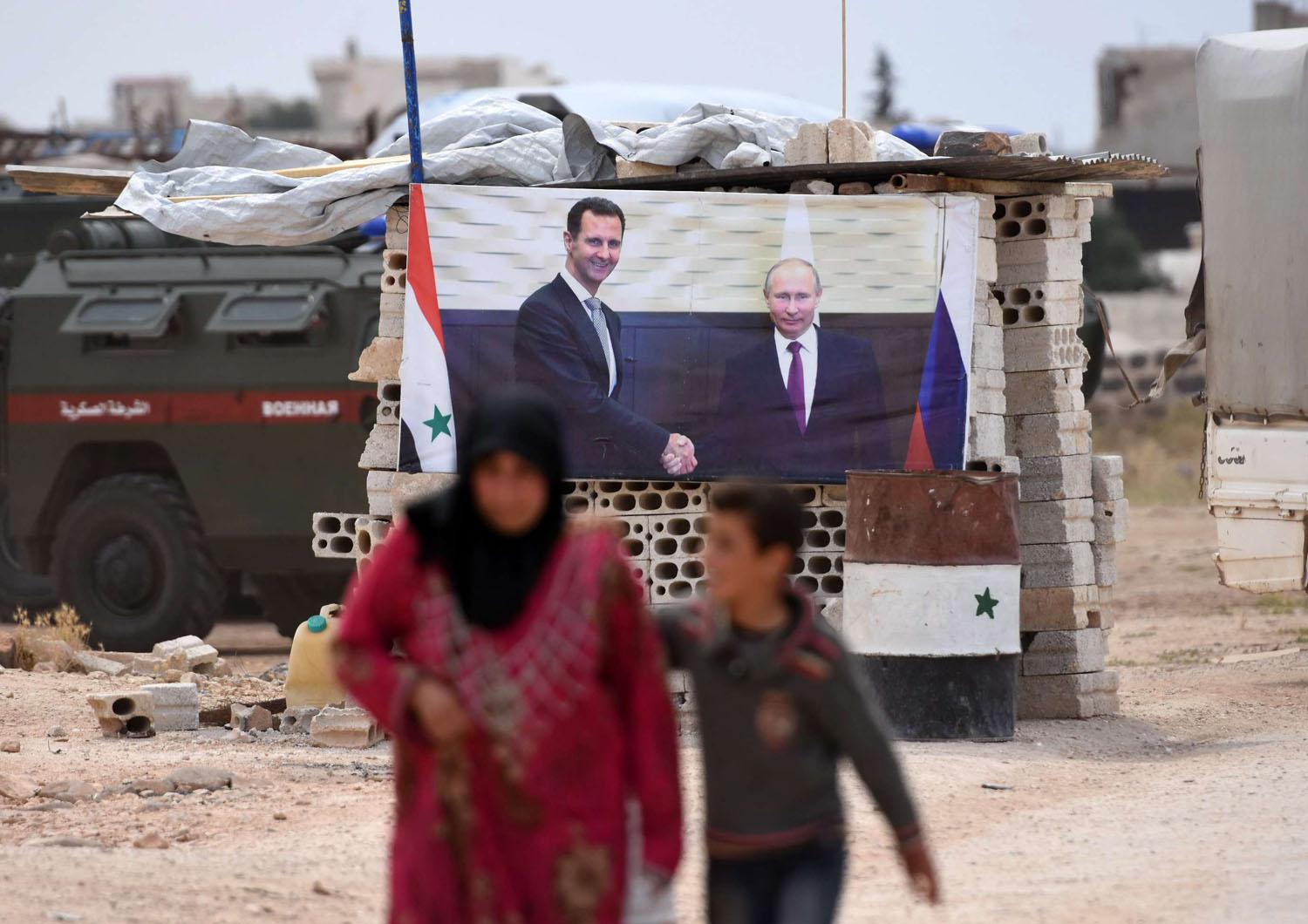 سيدة سورية تمر بجانب ملصق للرئيسين بوتين والأسد