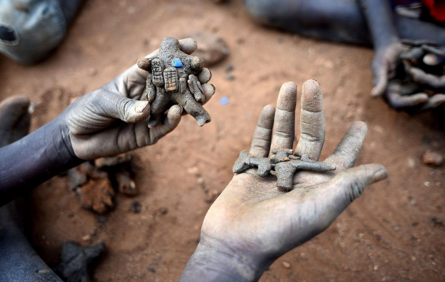 Displaced child holds clay model toys of a peacekeeper and a rifle in Juba, South Sudan.