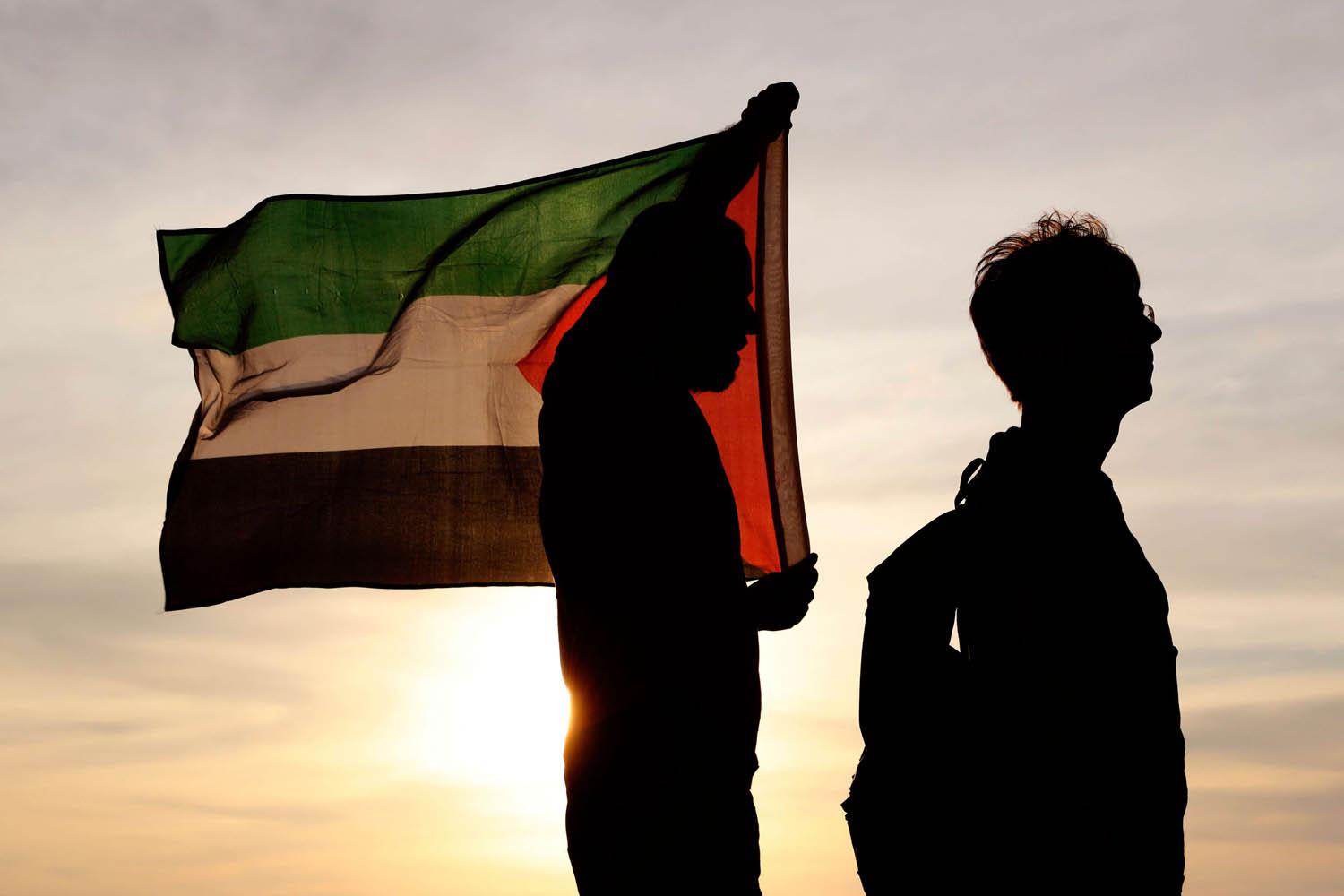 فلسطينيان يرفعان علم بلادهما قرب الحدود بين غزة وإسرائيل