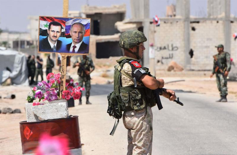 Members of Russian and Syrian forces stand guard near posters of Syrian President Bashar Assad (L) and his Russian counterpart Vladimir Putin at the Abu Duhur crossing on the eastern edge of Idlib, last August.