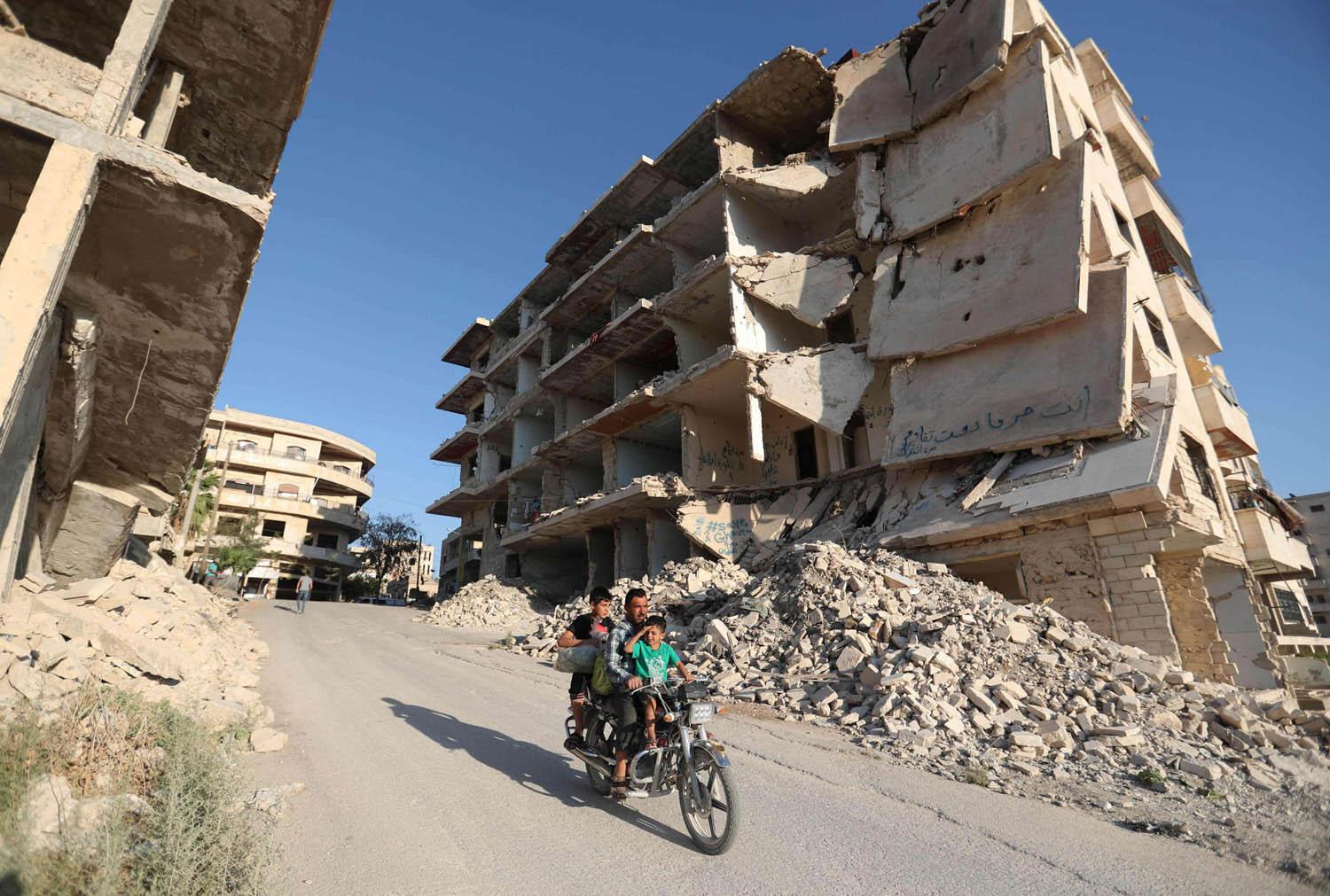 سوري يمر مع اطفاله بالقرب من أبنية مدمرة في معرة النعمان
