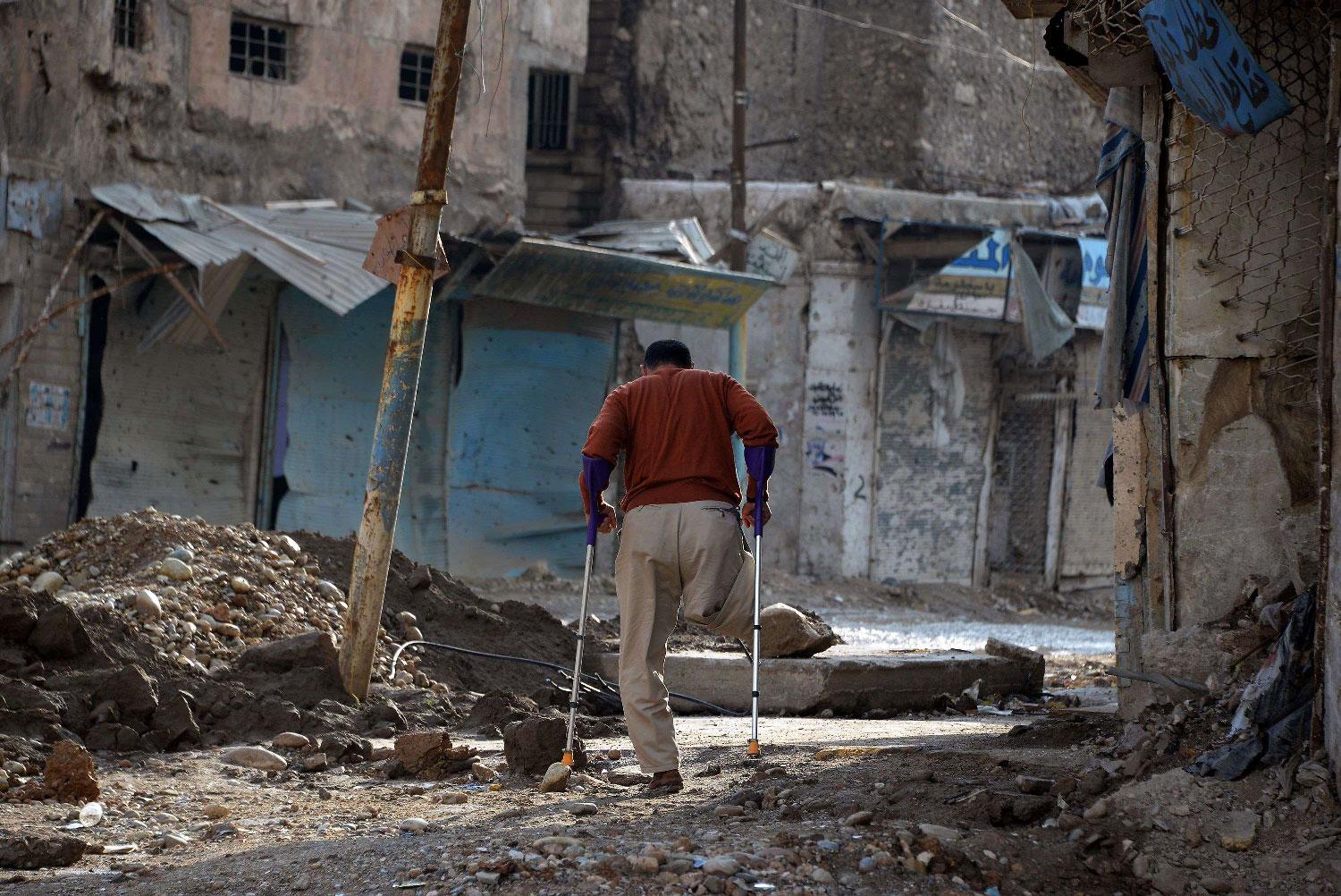 An amputee uses crutches to walk in a debris-strewn street in the old neighbourhood of the northern Iraqi city of Mosul on November 7, 2018.