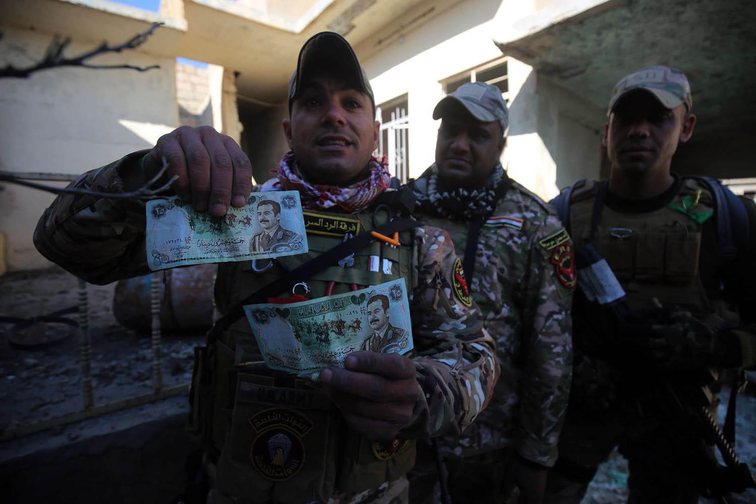 جنود عراقيون يعرضون عملة عراقية تحمل صورة الرئيس العراقي الراحل صدام حسين في قرية بالقرب من الموصل