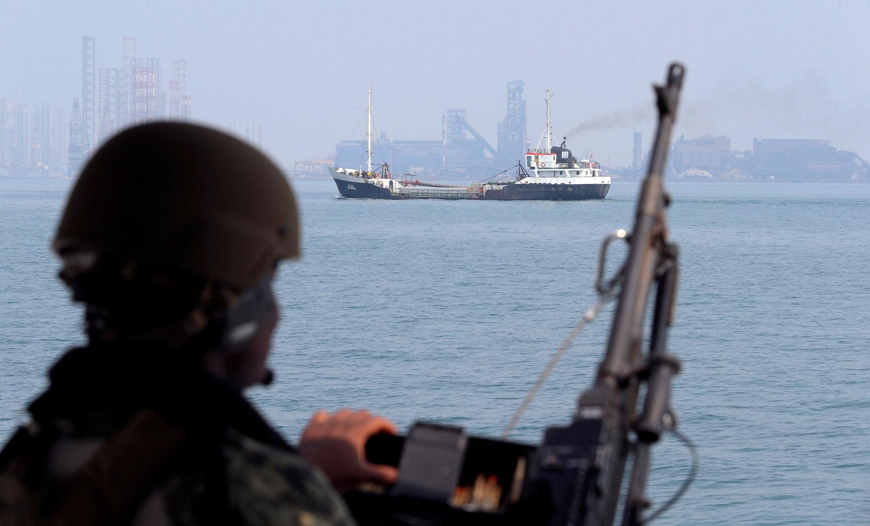 US Navy soldier stands guard as an oil tanker sails past.