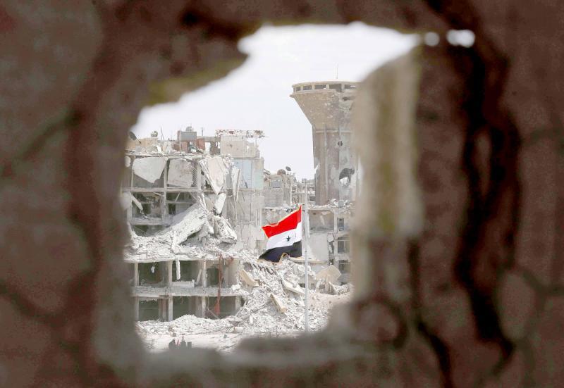 A Syrian flag flies in a rubble strewn street at the entrance of the Hajar al-Aswad neighbourhood on the southern outskirts of Damascus