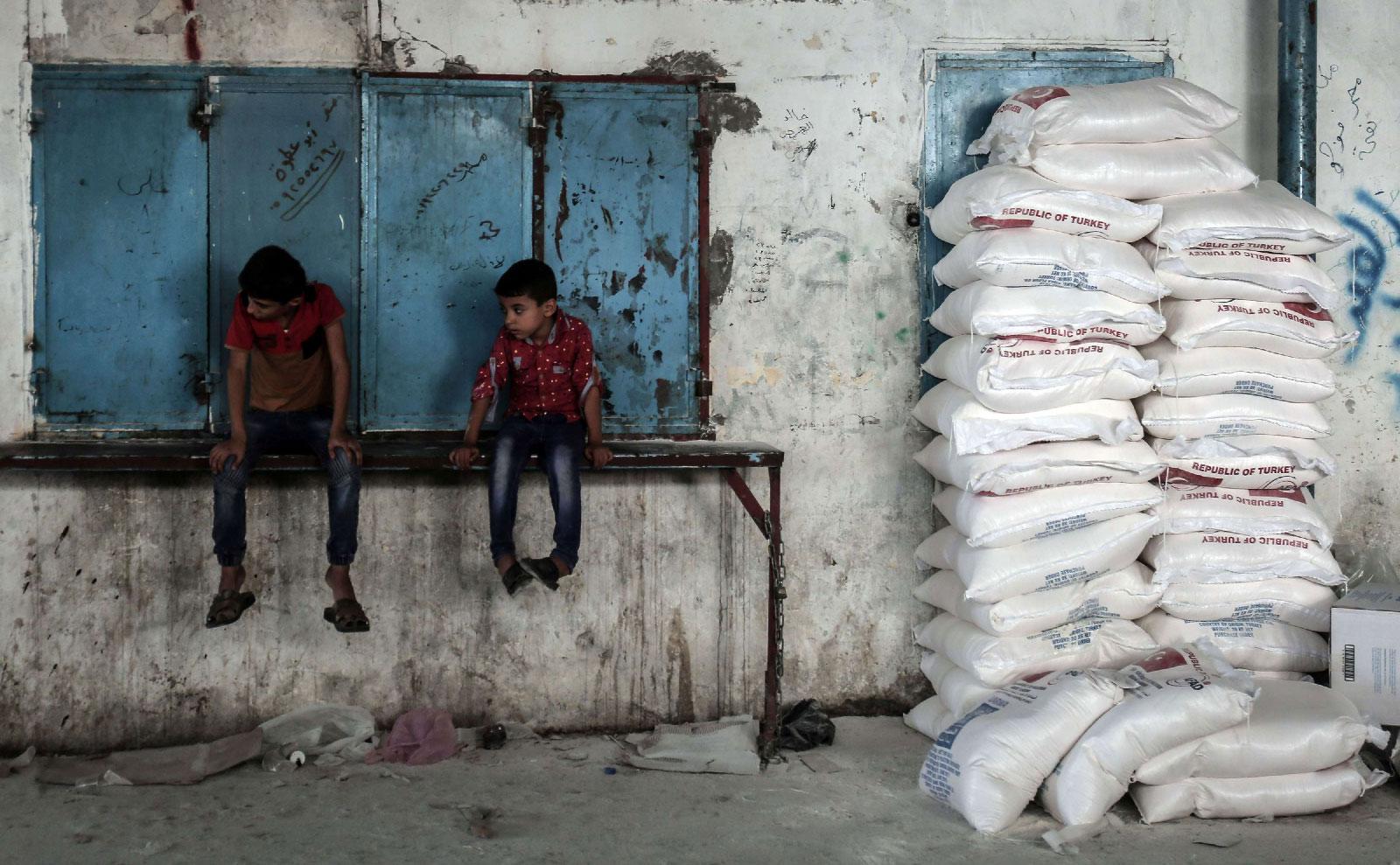 Palestinian children sit by sacks of food aid in the town of Rafah, southern Gaza Strip.