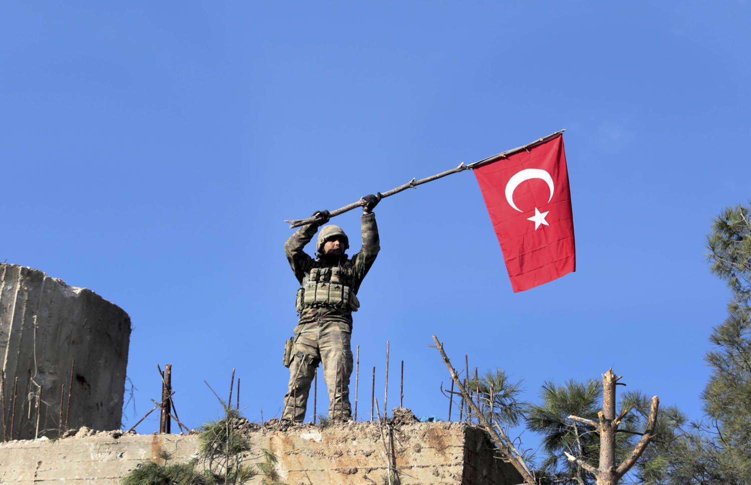 جندي تركي يرفع علم بلاده فوق سطح مبنى في بصيرة بالقرب من عفرين