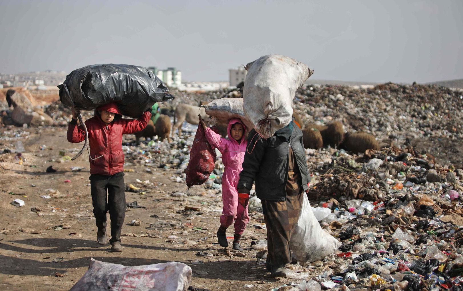 A displaced Syrian woman and children carry over their heads bags of collected trash at a landfill outside a camp in Kafr Lusin near the border with Turkey in Idlib province in northwestern Syria, on January 29, 2019.