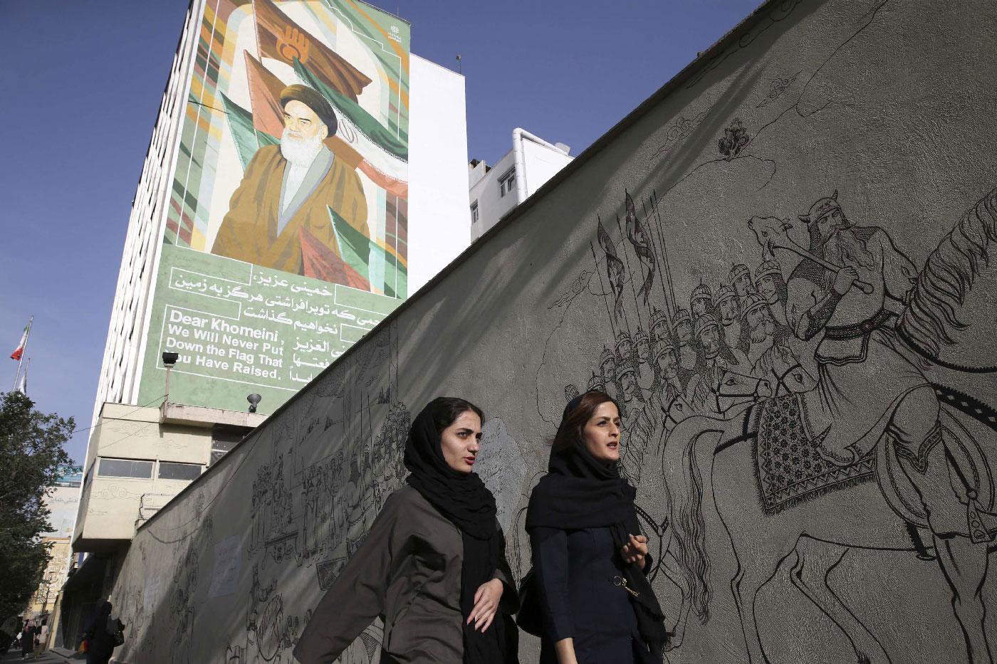 Iranian women walk past a portrait of the late revolutionary founder Ayatollah Khomeini and paintings of Persian poetry in Tehran, Iran, Monday, May 7, 2018.