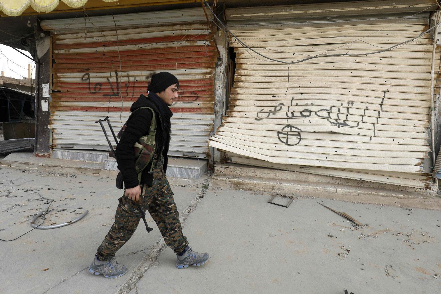 A fighter from the Syrian Democratic Forces (SDF) walks past shops with their fronts painted with the Arabic phrases "beware a sniper" and "caliphate state", in the city of Hajin in Syria's eastern Deir Ezzor province on January 27, 2019.