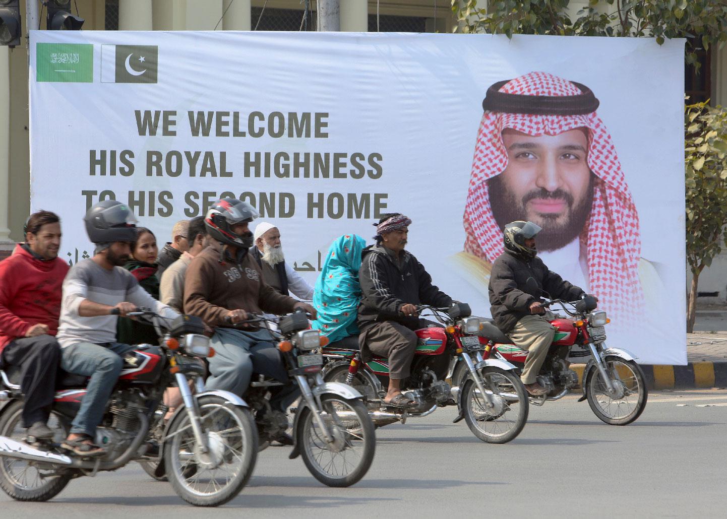 Pakistani motorcyclists pass by a banner welcoming Saudi Arabia's Crown Prince Mohammed bin Salman displayed on the occasion of his visit, in Lahore, Pakistan, Saturday, Feb. 16, 2019.