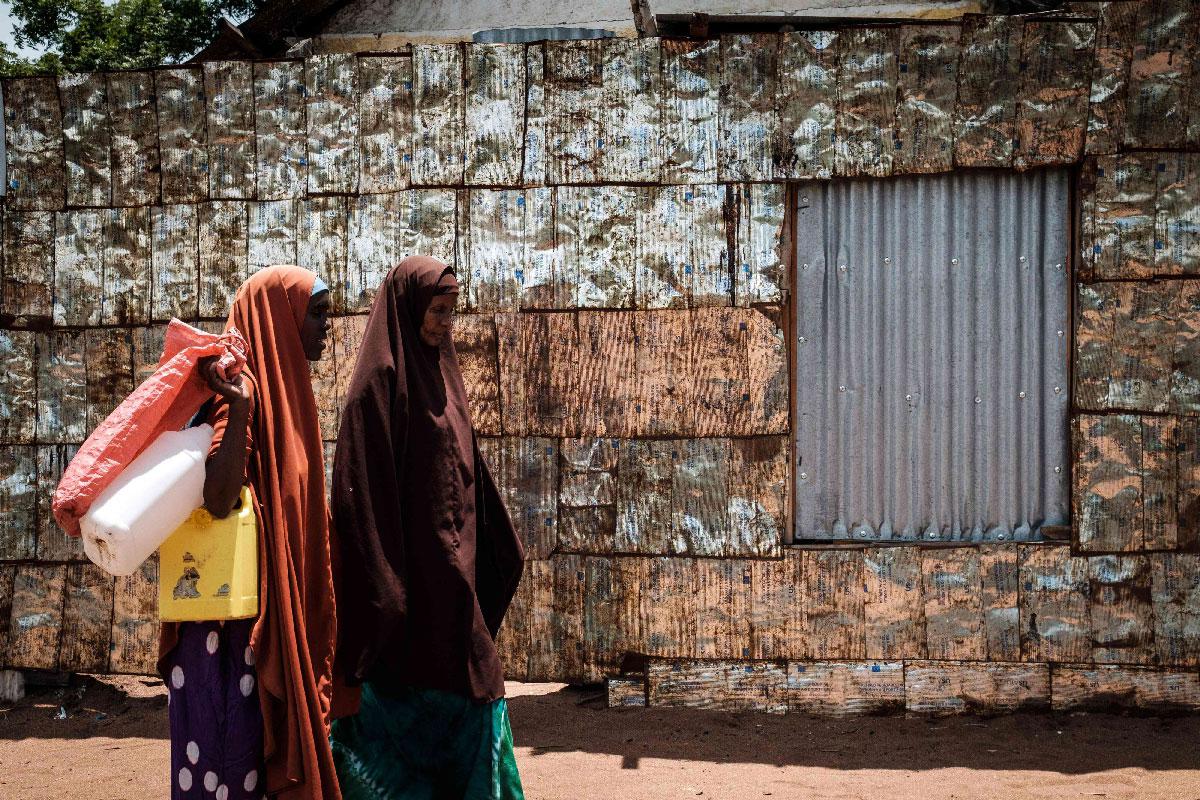 Women walk in front of a metal fence made of vegetable oil cans from USAID at the Dadaab refugee complex, northeastern Kenya, on April 18, 2018.