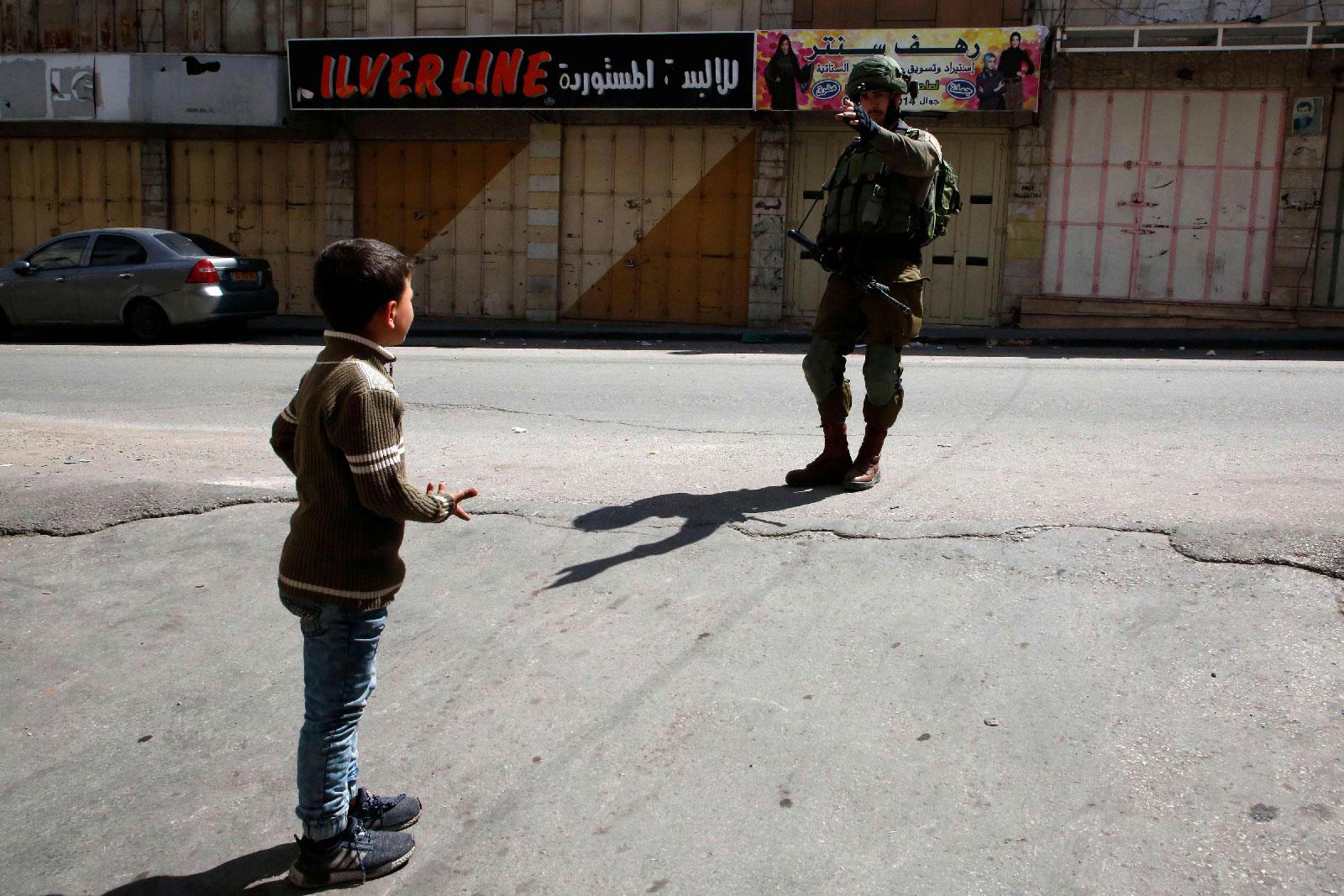 A Palestinian boy is denied access to a street by an Israeli soldier in the occupied West Bank city of Hebron on March 2, 2018, as it's closed for the visit of Jewish settlers to what they believe is the tomb of biblical figure Othniel Ben Kenaz.