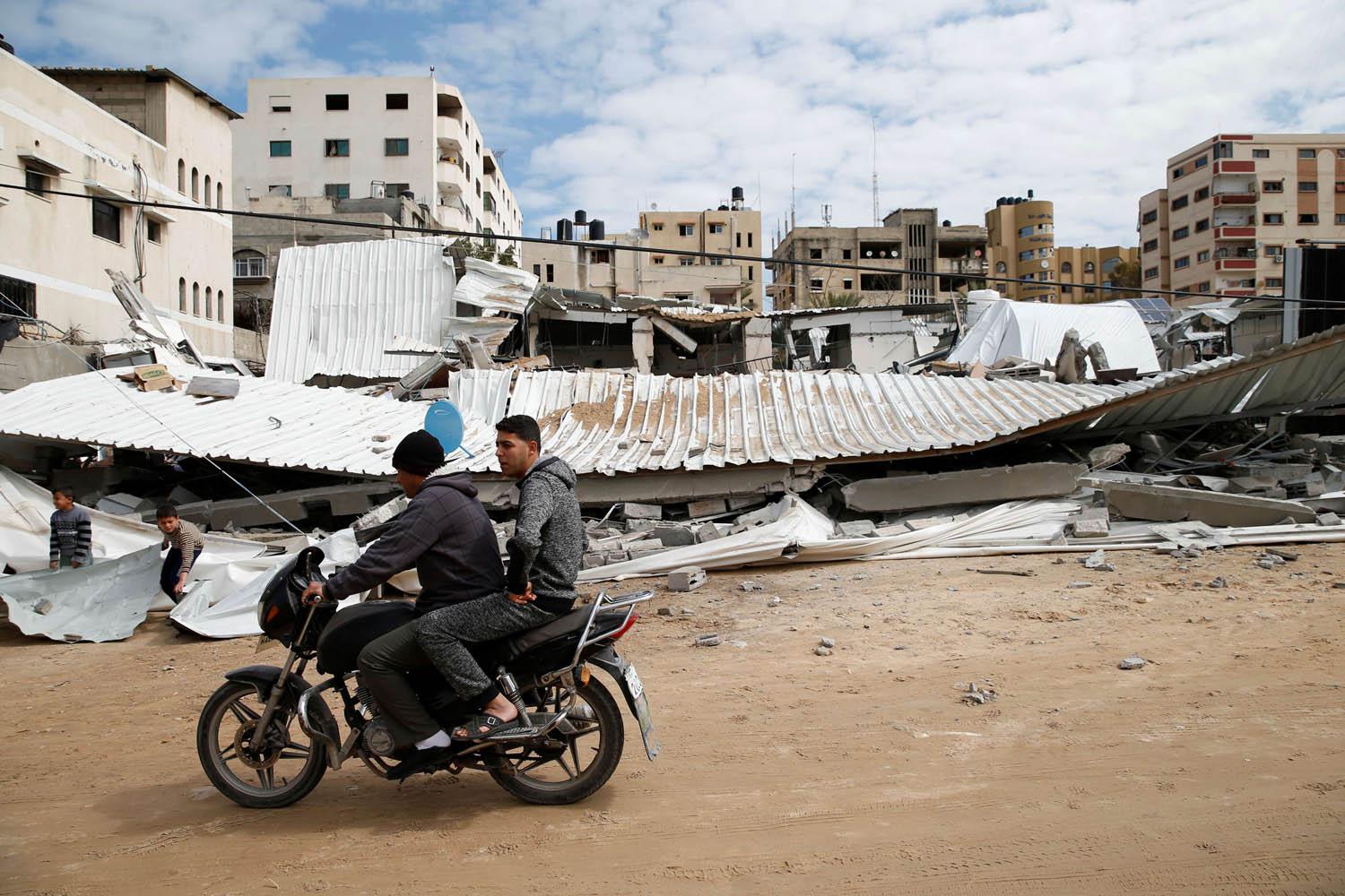 فلسطينيان يمران على دراجة بالقرب من مبنى دمرته اسرائيل بقصف جوي على غزة 