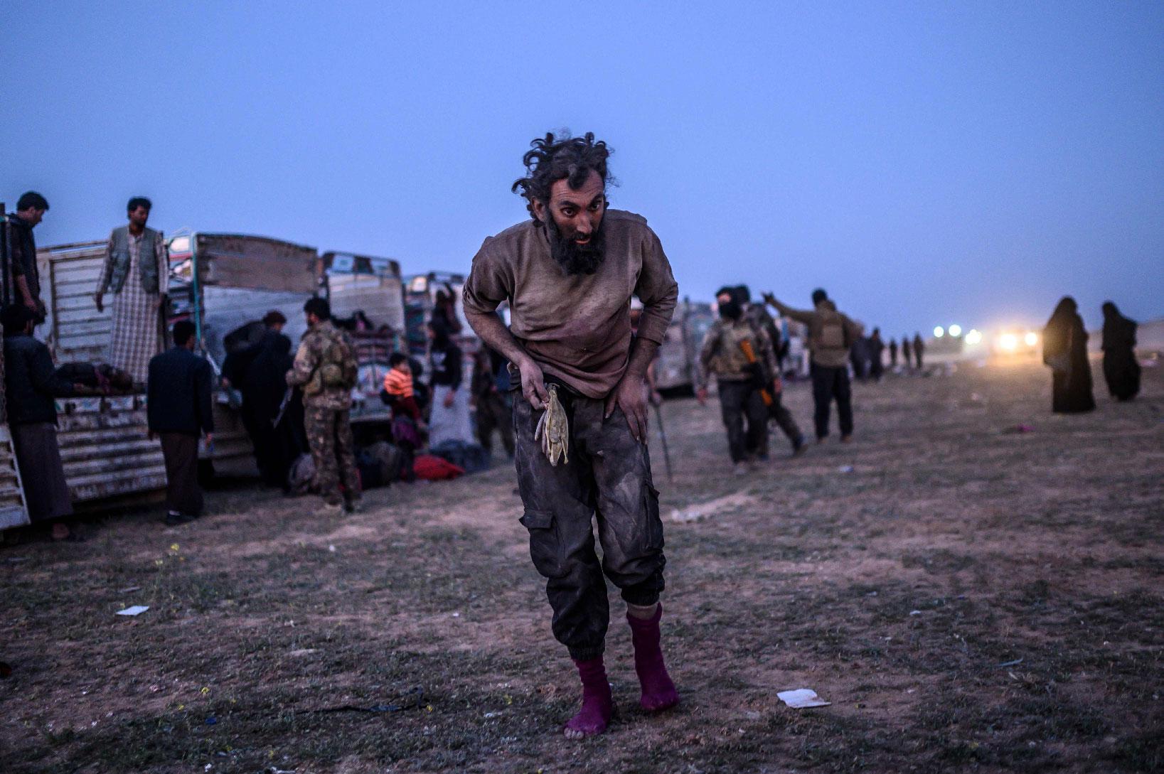 A man suspected of belonging to the Islamic State (IS) group walks past members of the Kurdish-led Syrian Democratic Forces (SDF) just after leaving IS' last holdout of Baghouz, in the eastern Syrian province of Deir Ezzor on March 4, 2019.