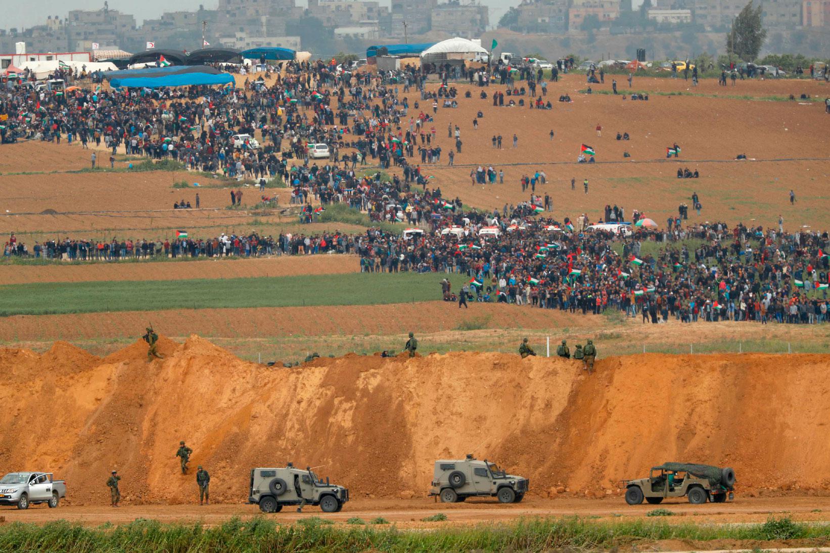 In this file photo taken on March 30, 2018 from the southern Israeli kibbutz of Nahal Oz across the border from the Gaza Strip, Palestinians participating in a tent city protest commemorating Land Day, with Israeli military vehicles seen below in the foreground.