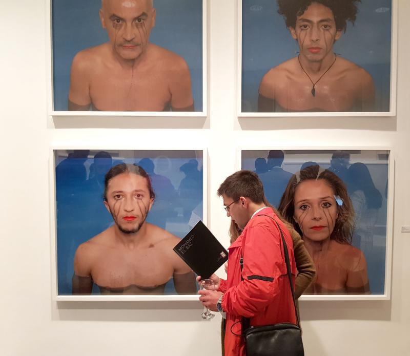 Visitors go through a booklet at the solo exhibition of Moroccan contemporary artist Mohamed El Baz in Casablanca