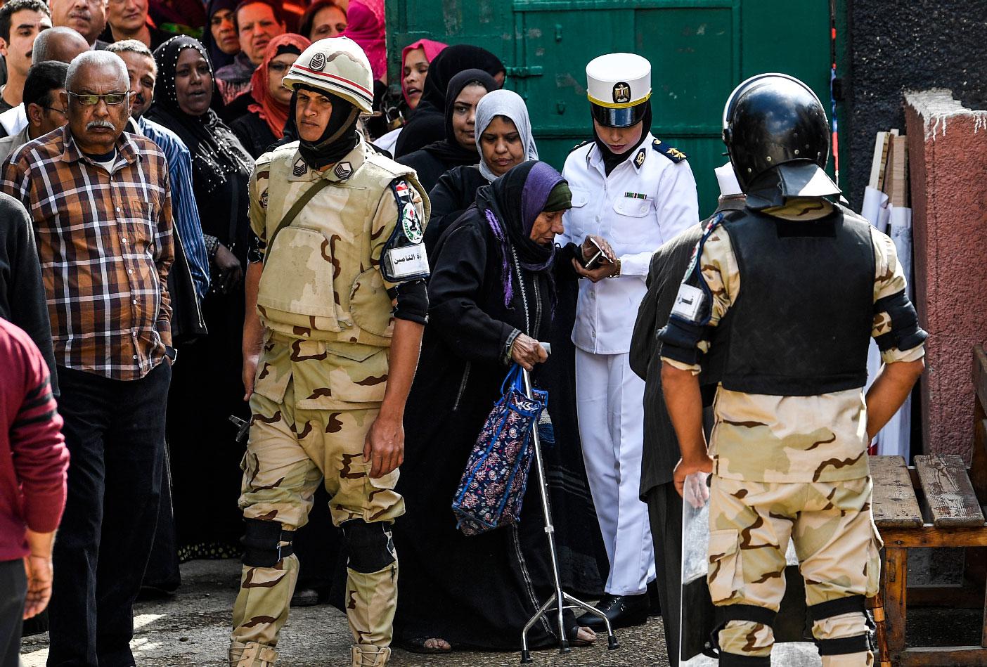 An Egyptian policewoman helps an elderly voter as she arrives at a polling station