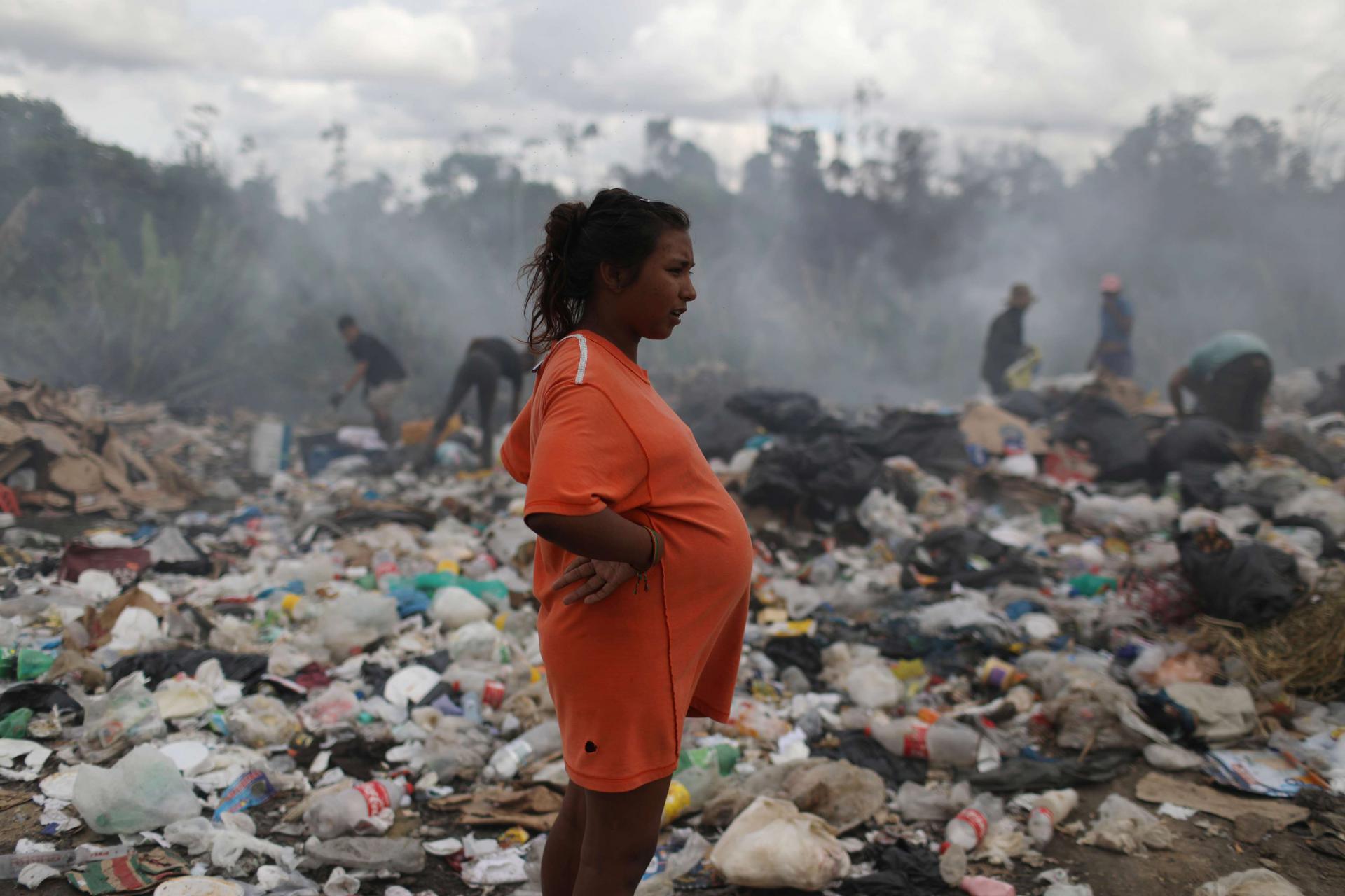 امرأة حامل تقف قرب مصب نفايات يتصاعد منه الدخان