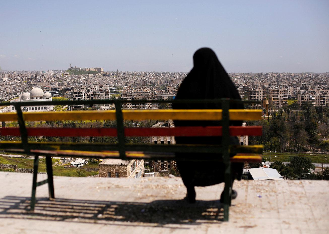 A woman sits on a bench overlooking Aleppo's ancient citadel and the old city