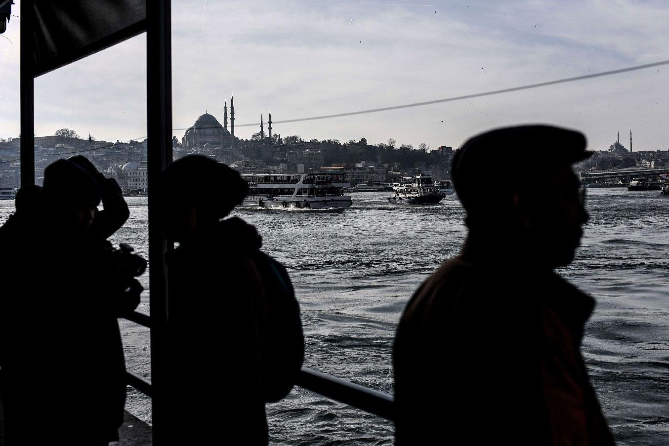 People stand on Galata bridge in Istanbul as Suleymaniye mosque is seen in the background