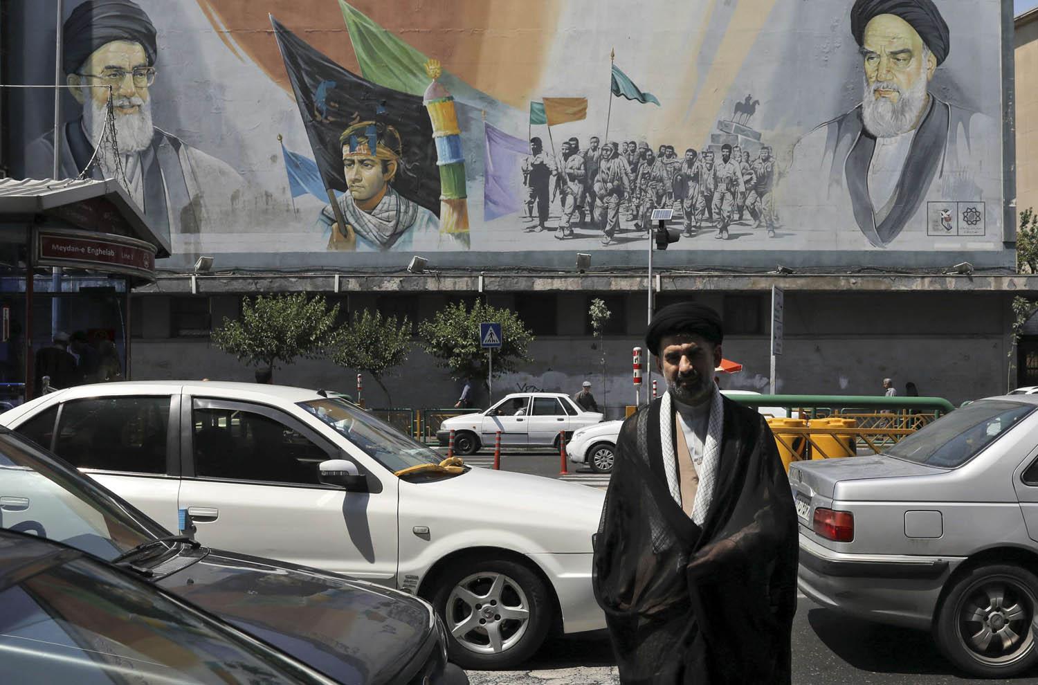 ملا إيراني وسط طهران مع جدارية للخميني وخامنئي