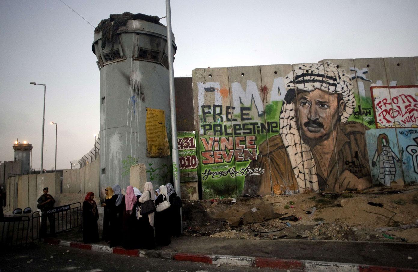 Palestinian women wait near a section of Israel's separation barrier