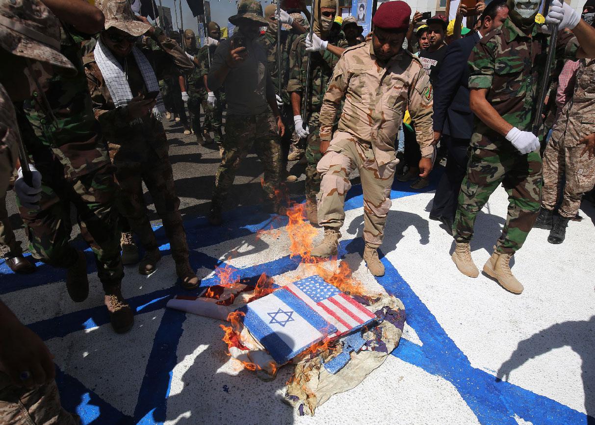 Iraqi Shiite fighters from the Iran-backed armed group, Hezbollah brigades, burn US and Israeli flags