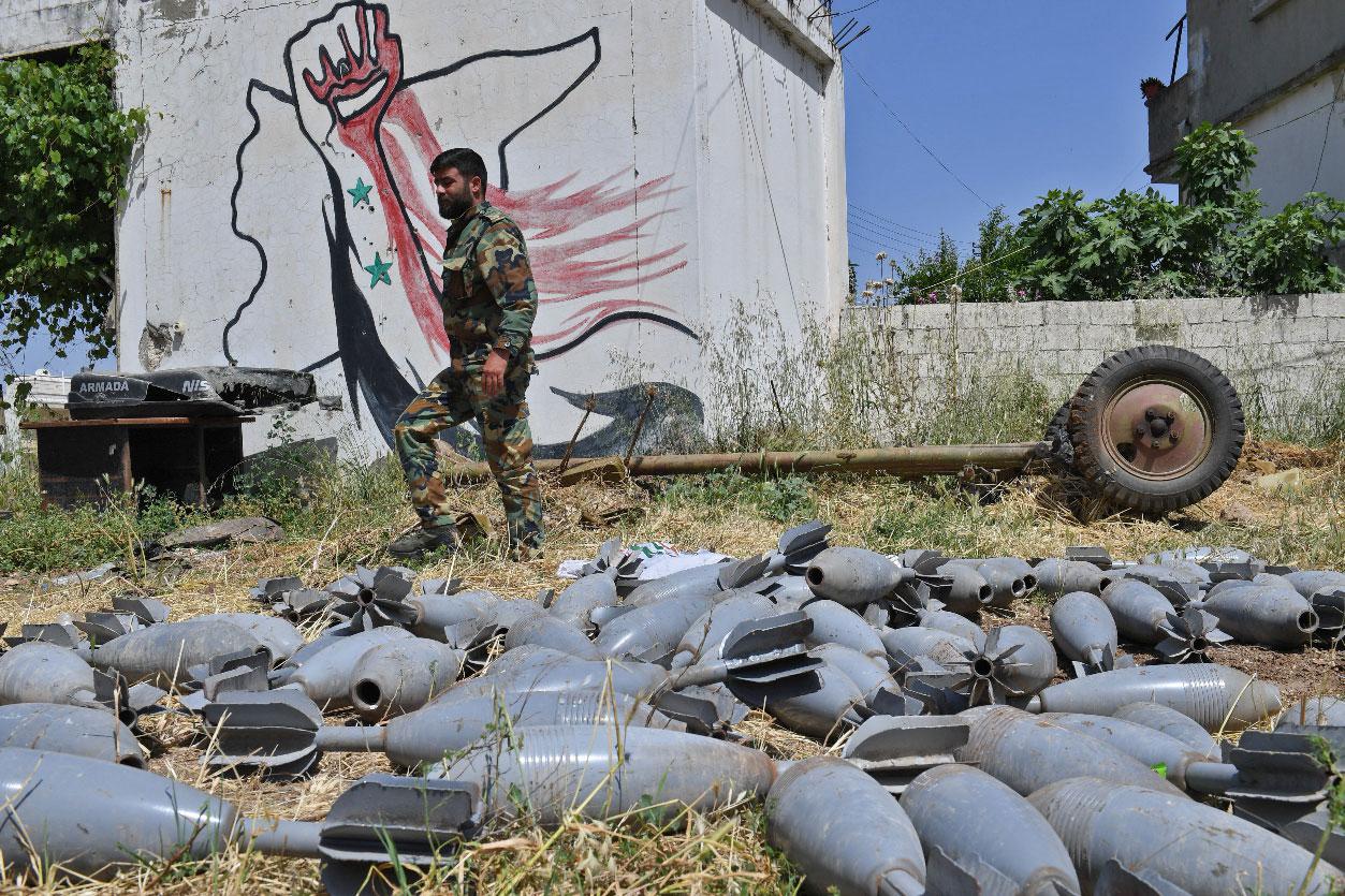 A Syrian government soldier walks past mortar shells in the village of Qalaat al-Madiq