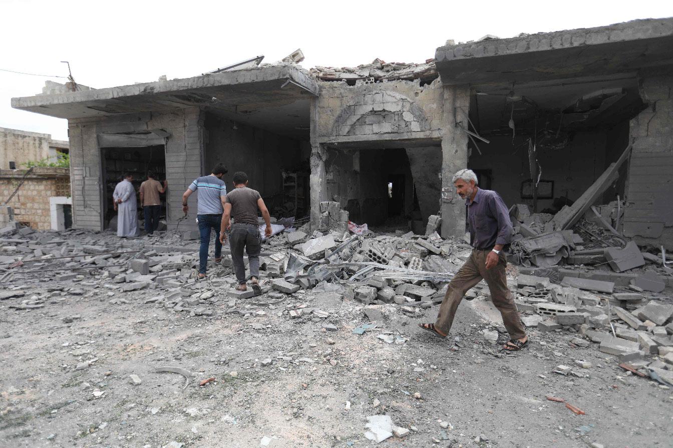 People walk past destruction at the scene of an area targeted by regime airstrikes