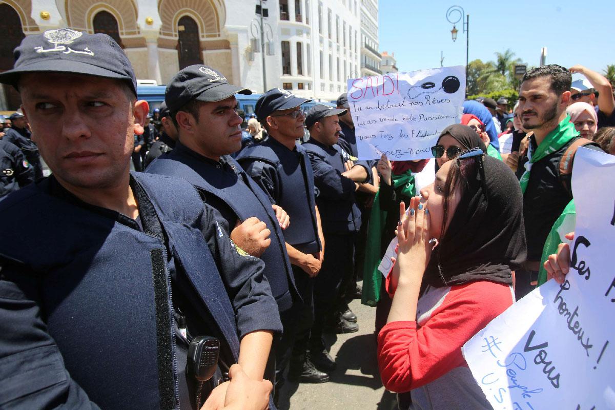 Police officers stand guard as students chant slogans during a protest demanding the removal of the ruling elite in Algiers