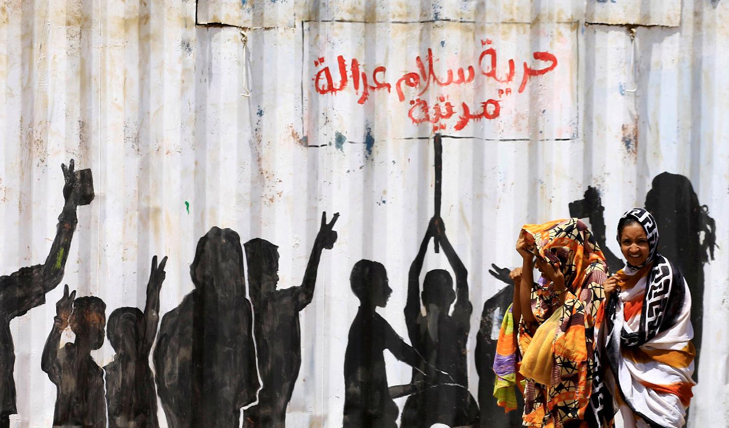 Civilians walk past graffiti reading in Arabic "Freedom, Peace, Justice and Civilian" in the Burri district of Khartoum