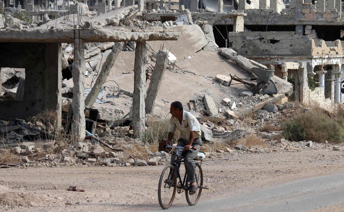 A Syrian man rides a bicycle past destroyed buildings in an opposition-held neighbourhood of the southern city of Daraa