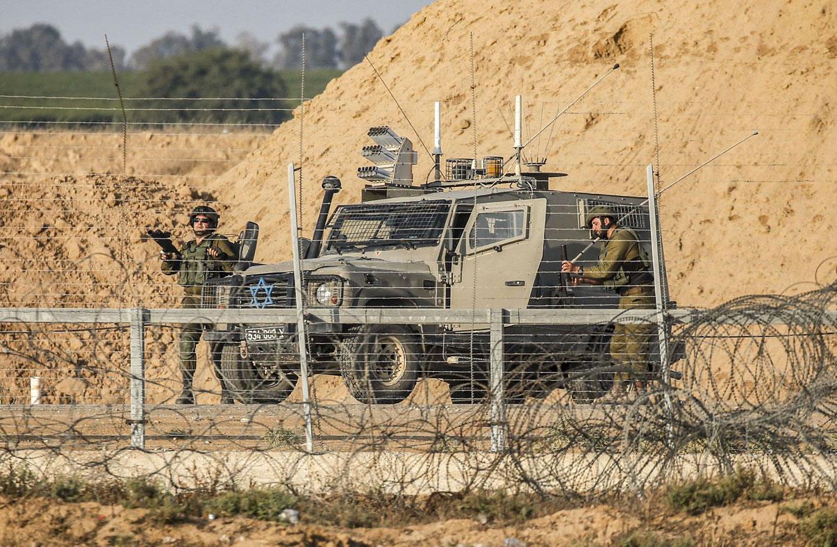 Israeli soldiers are seen next to a military vehicle across the barbed-wire fence with the Gaza Strip