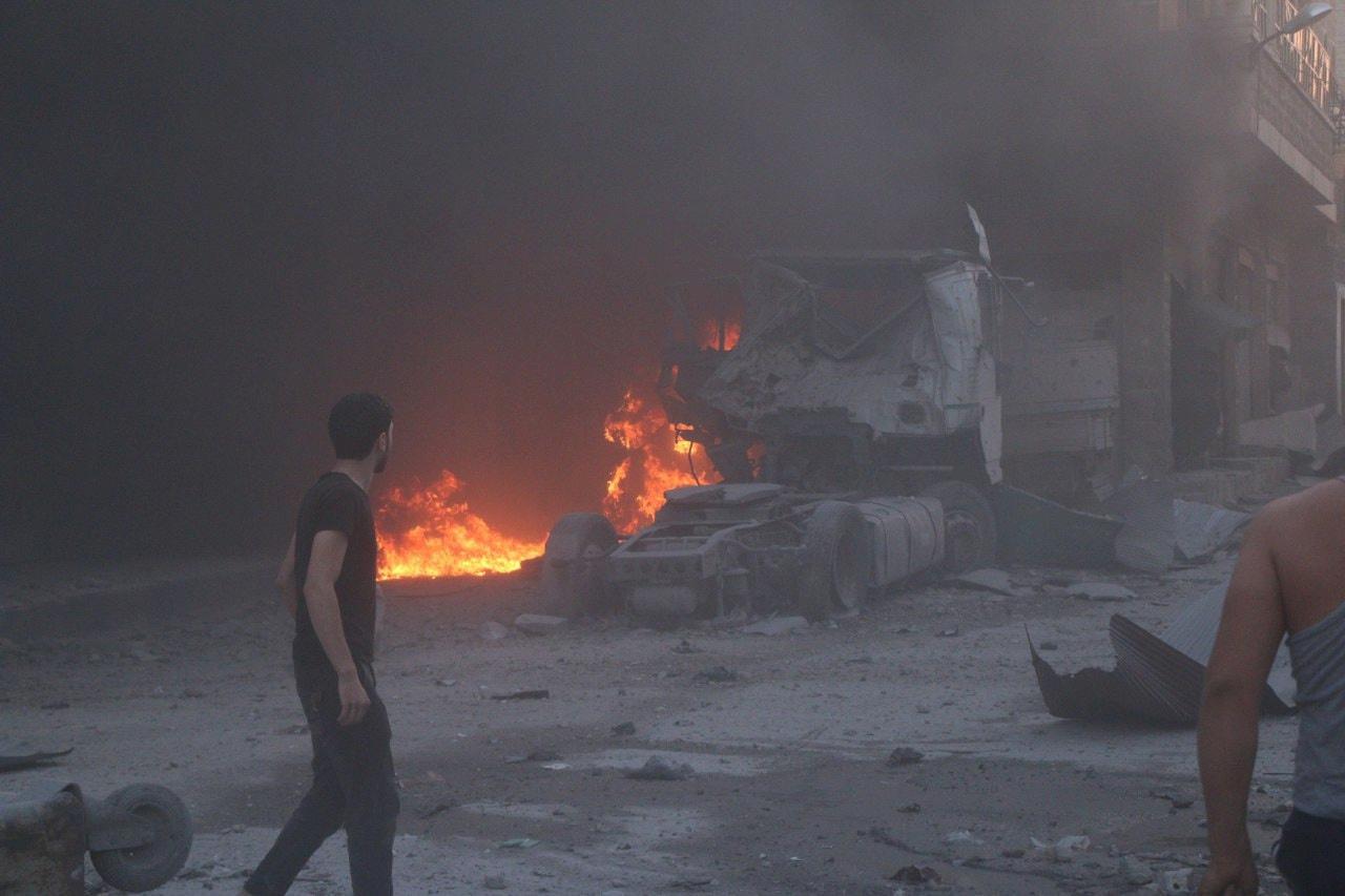 People walk next to fire, debris and a damaged truck after a deadly airstrike in Idlib province