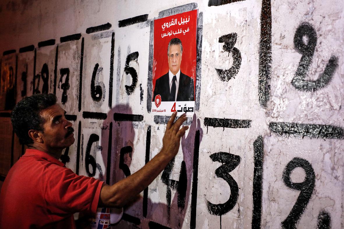 A supporter of the Tunisian businessperson and media mogul Nabil Karoui sticks a campaign poster to a wall